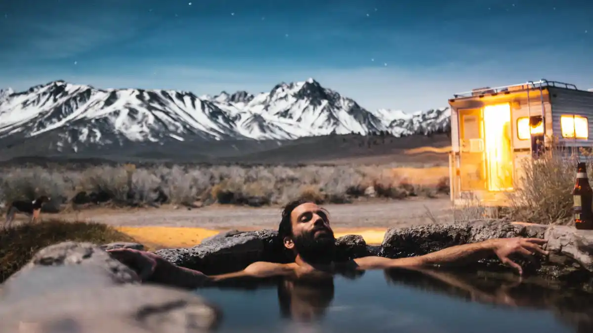 man relaxing in a hot spring in the open air with snow covered mountains as a backdrop.